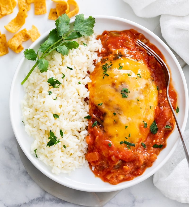 A white plate with Salsa Chicken on it next to white rice with a cilantro garnish.