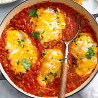 Salsa Chicken in a skillet with salsa, melted cheese, and cilantro with a wooden spoon on the side.