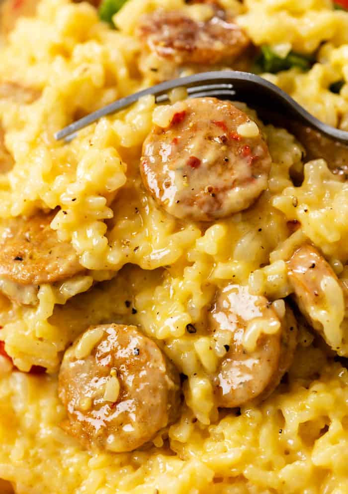 Cheesy rice with slices of cooked sausage and a fork in the background.