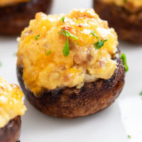 A Sausage Stuffed Mushroom on a white plate with fresh parsley on top.