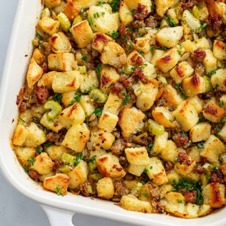 A white casserole dish with sausage stuffing with parsley on top.