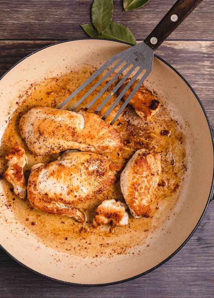 Overhead view of seared chicken in a cast iron skillet with a spatula.