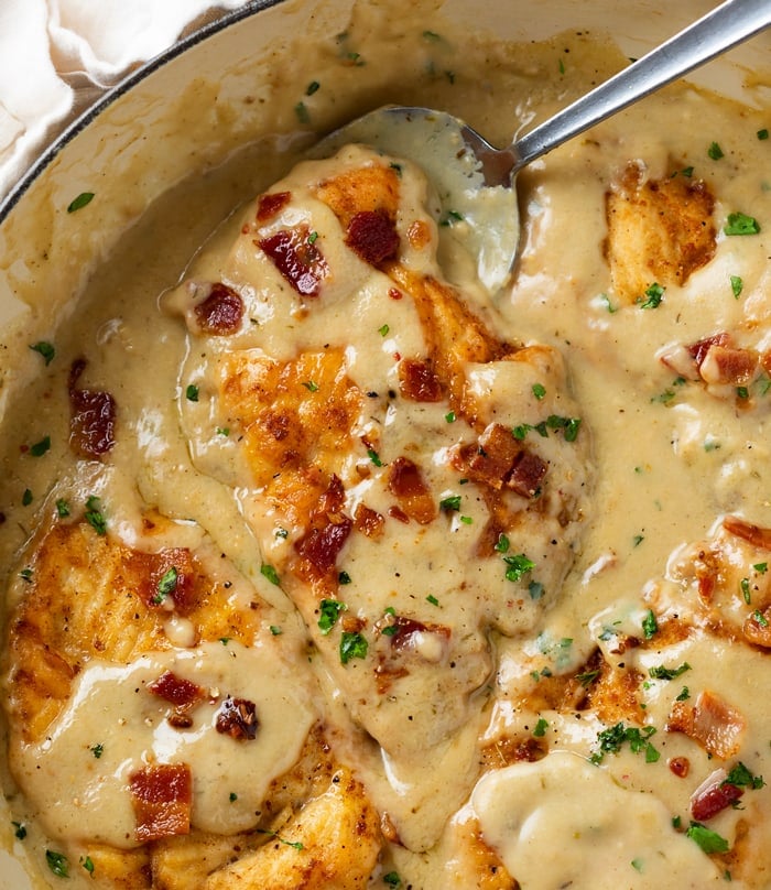 A skillet with Smothered Chicken in gravy topped with crispy bacon and parsley.