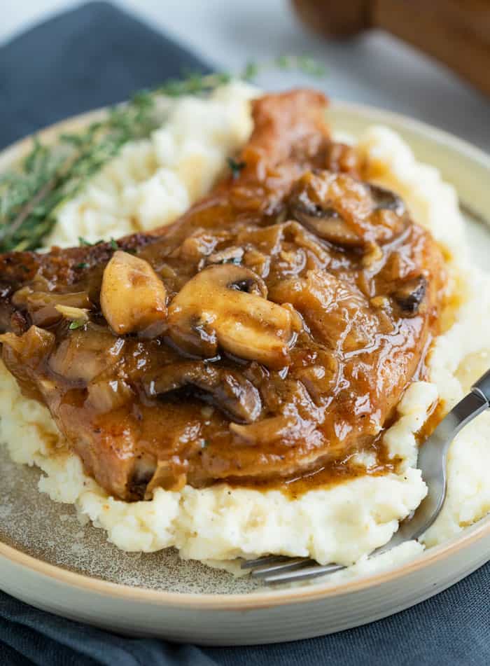 White potatoes on a plate topped with a pork chop smothered in a french onion sauce with mushrooms.