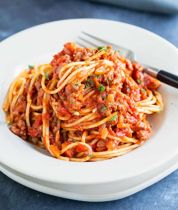 A white bowl filled with spaghetti Bolognese with a fork in the background.