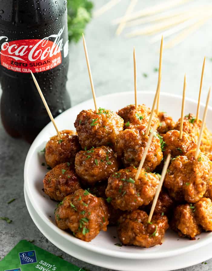 White plate filled with spicy sausage bites and a coca-cola zero sugar bottle in background.