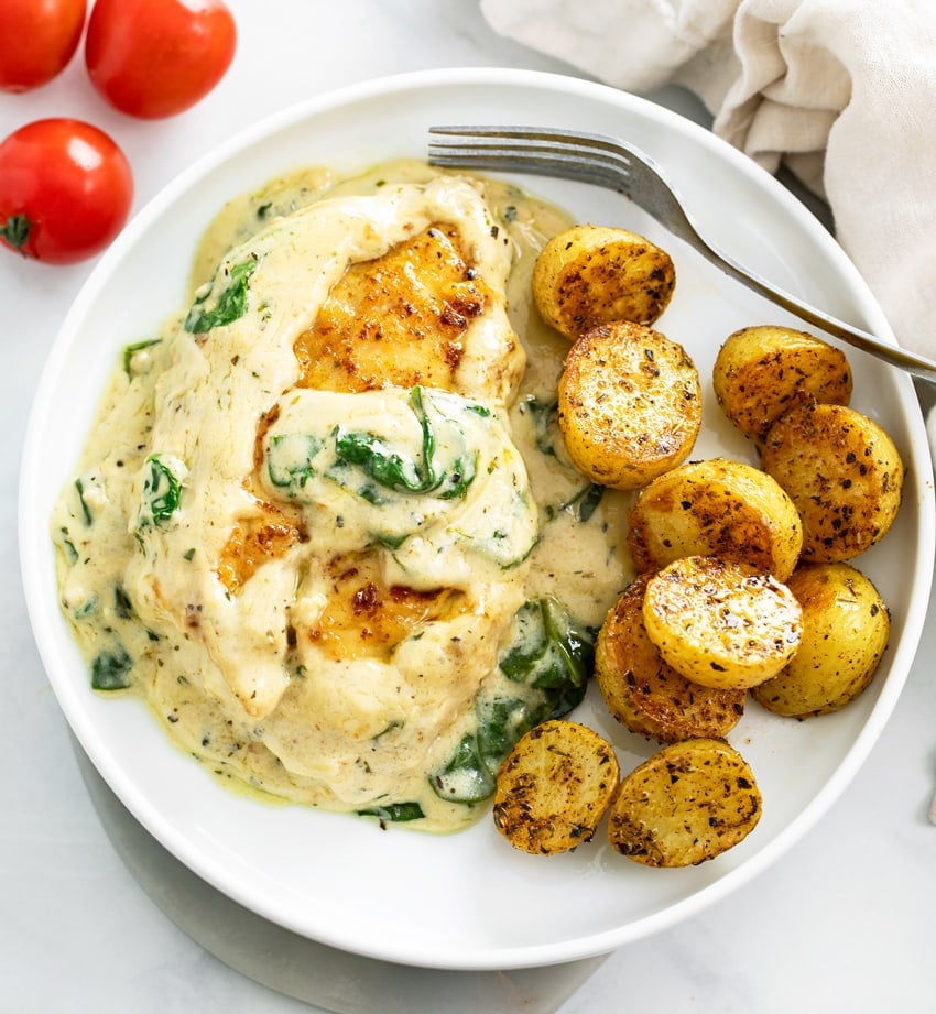 Creamy Spinach Chicken on a white plate with roasted potatoes and a fork.