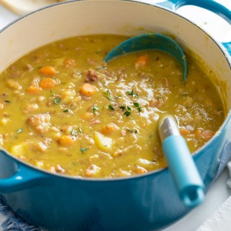 A pot of Split Pea Soup with a ladle in it and fresh thyme on top.