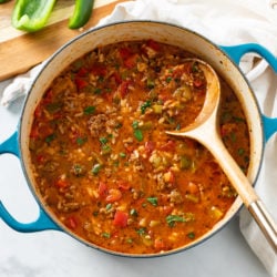 A soup pot filled with Stuffed Pepper Soup with a wooden spoon in it.