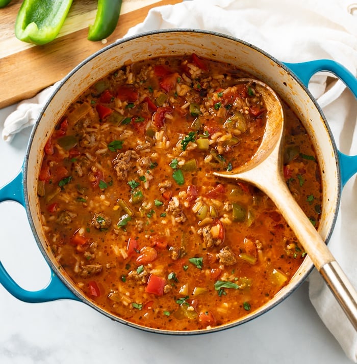 A soup pot filled with Stuffed Pepper Soup with a wooden spoon in it.