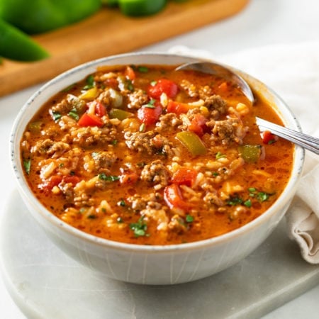 A bowl of Stuffed Pepper Soup with a spoon in it and bell peppers in the background.