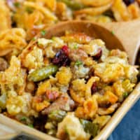 A casserole dish with a wooden spoon scooping out stuffing casserole with green beans.