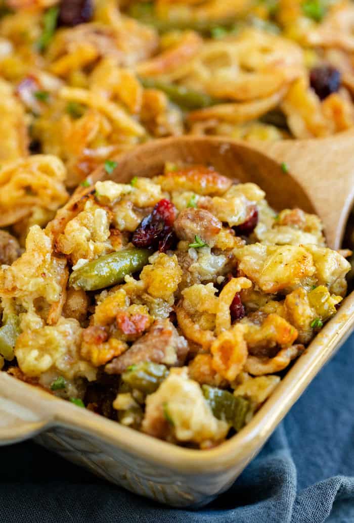 Stuffing and green bean casserole being scooped up with a wooden spoon.