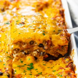 A casserole dish filled with Taco Lasagna that's being pulled up with a spatula.