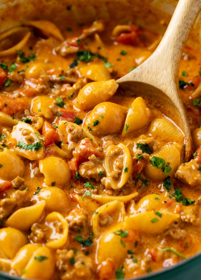 A wooden spoon scooping up taco pasta from a pot.