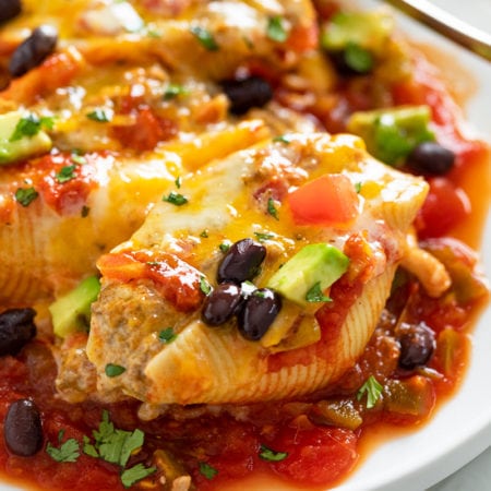 Taco Stuffed Shells on a white plate with cheese, black beans, and avocado.