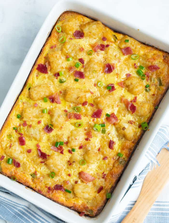 A white casserole dish with tater tot breakfast casserole topped with bacon.