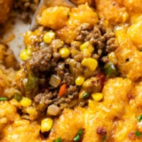 A spoon scooping up Tater Tot Casserole from a skillet with crispy tater tots and ground beef with corn.