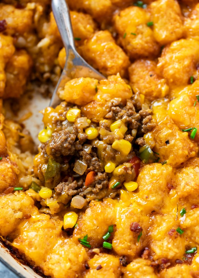 A spoon scooping up tater tot casserole with ground beef, corn, and crispy tater tots.