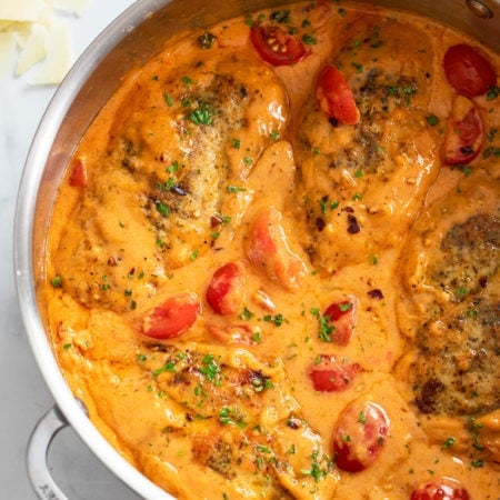 Tomato Chicken in skillet filled with creamy tomato cream sauce and cherry tomatoes.