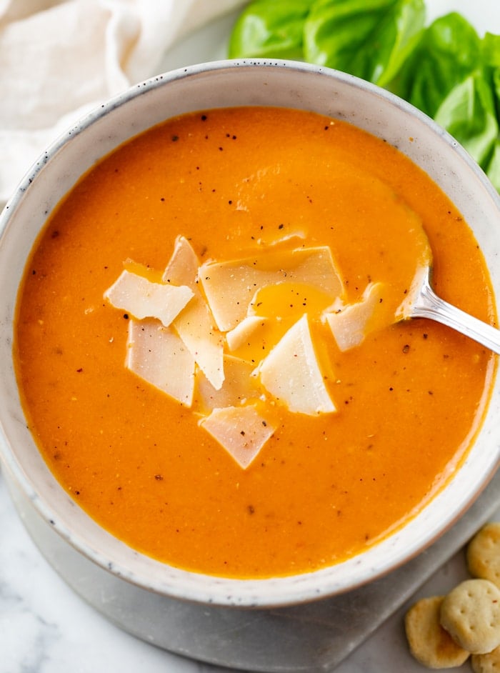 A bowl with Tomato Soup topped with shaved Parmesan Cheese with a spoon.