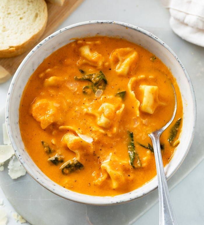 A white bowl with creamy Tomato Tortellini Soup in it with spinach.