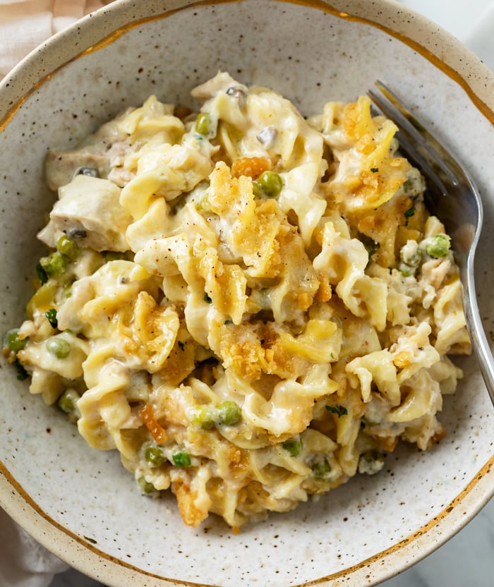 A bowl of Tuna Noodle Casserole with egg noodles in cream sauce with peas and crushed Ritz on top.