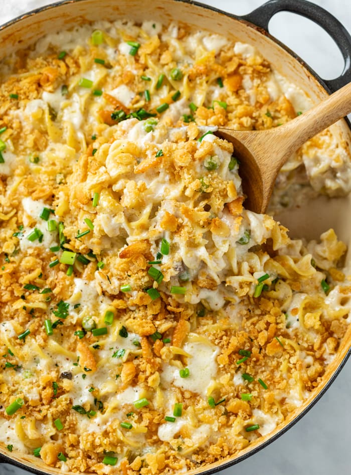 A round casserole dish with a wooden spoon scooping up Tuna Noodle Casserole topped with Ritz crackers.