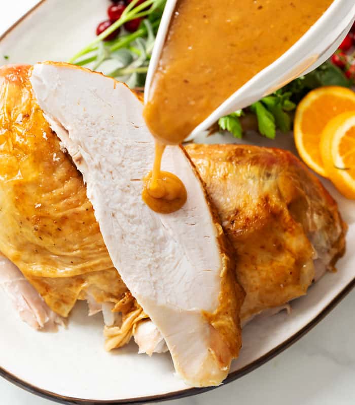 Brown turkey gravy being poured on top of turkey breast.