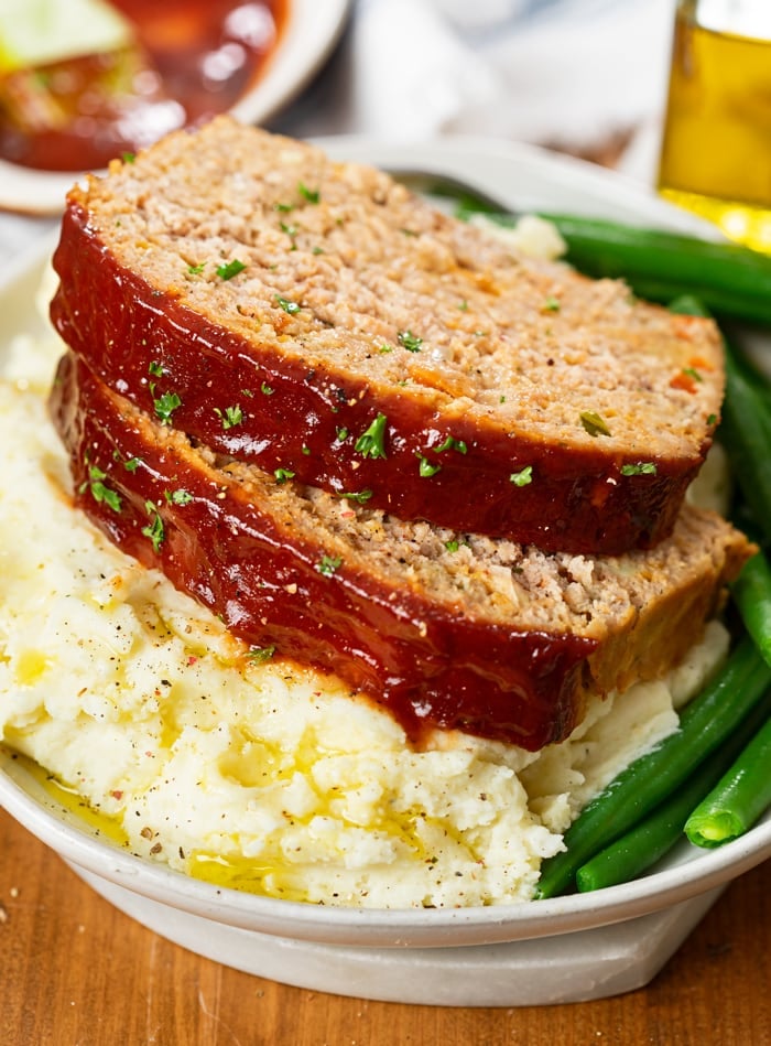 Slices of turkey meatloaf on top of mashed potatoes with green beans.