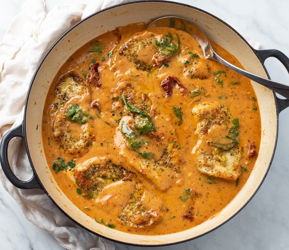 A skillet filled with Tuscan Chicken in sauce with sundried tomatoes and spinach.