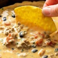 A hand dipping a Tortilla Chip into Velveeta Queso