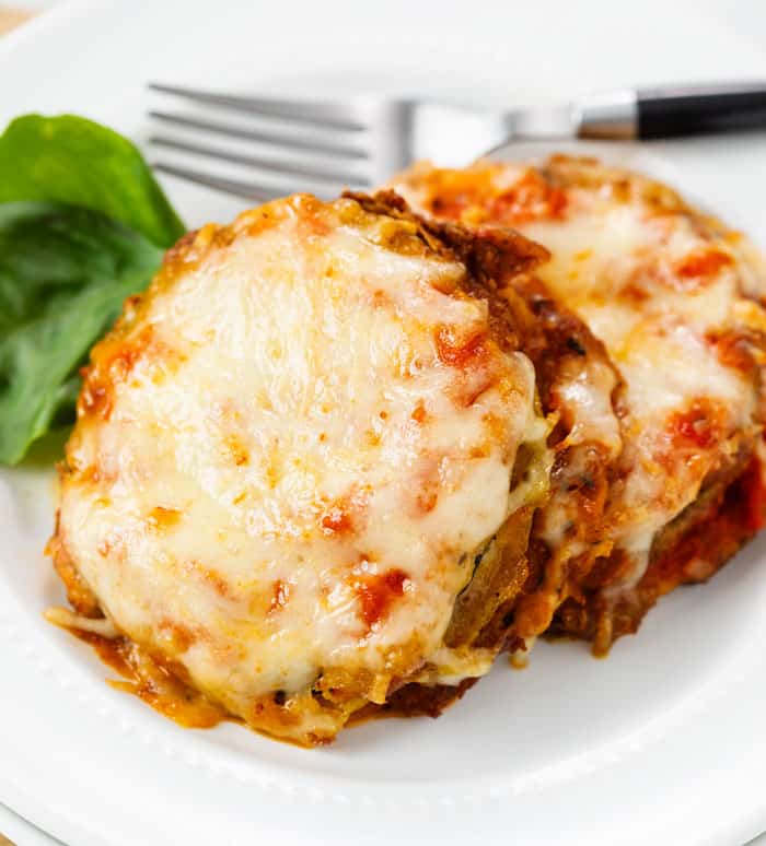 A white plate with slices of cheesy Zucchini Parmesan on it with a fork in the background.